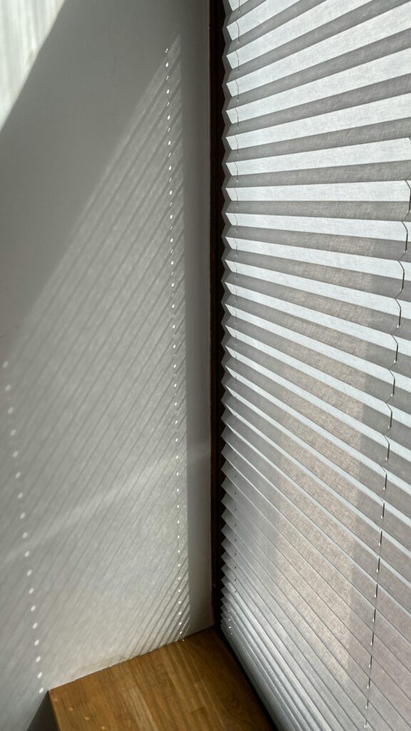 Sunlight creates captivating shadows on a wall through a modern roller blind.